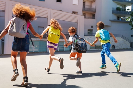 Kids running and holding hands with backpacks on.